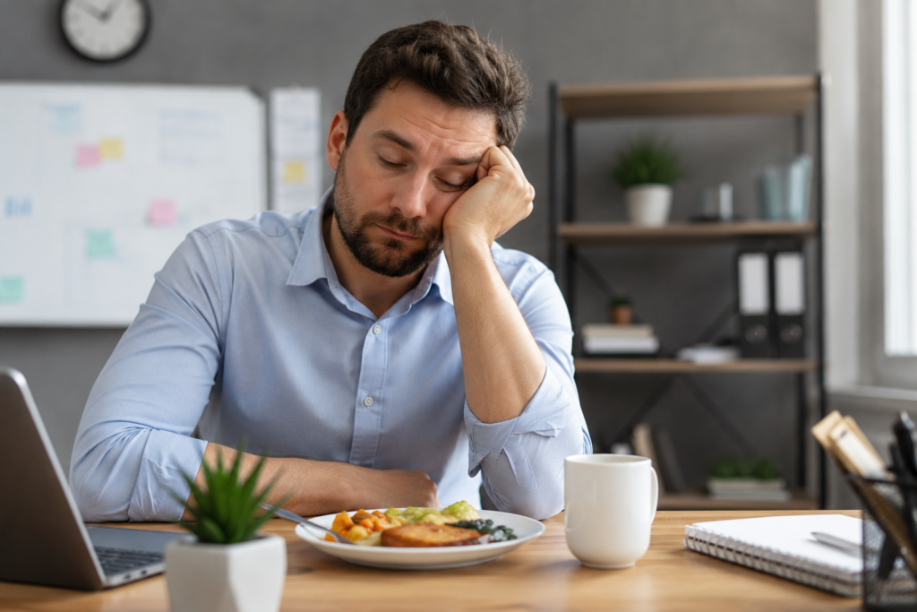 Tired person feeling low energy after eating food while sitting at office desk